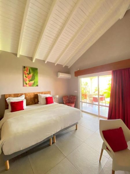 Habitación doble con cama grande, almohadas rojas y terraza exterior en Hôtel Le Soleil Levant