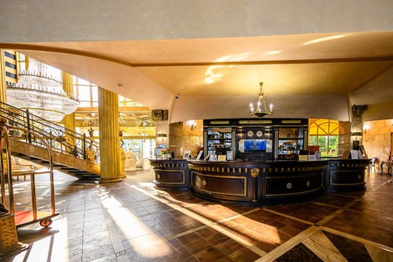 Recepción principal con mostrador clásico y escalera de lujo en el Imperial Palace Hotel