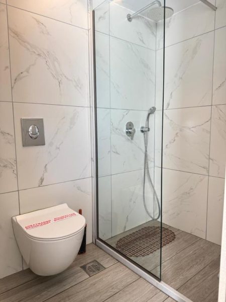 Baño moderno con ducha de cristal y revestimiento de mármol blanco en Crystal Beach Hotel