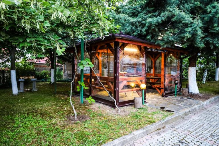 Pérgola acristalada con mesas de madera en el jardín exterior del Edi Hotel