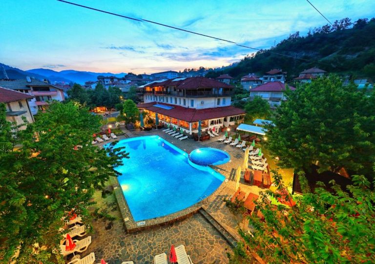 Vista aérea de la piscina exterior iluminada del Edi Hotel rodeada de tumbonas y vegetación al atardecer