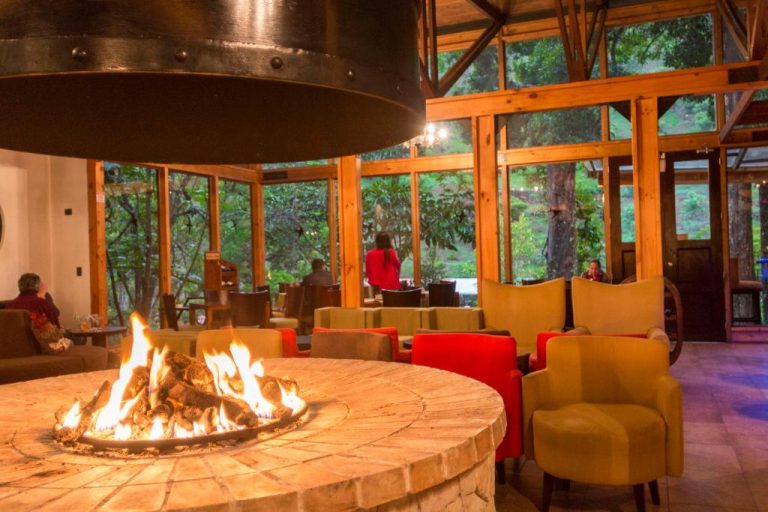 Salón con chimenea central y sillones junto a ventanales con vistas al bosque en Savegre Hotel Natural Reserve & Spa