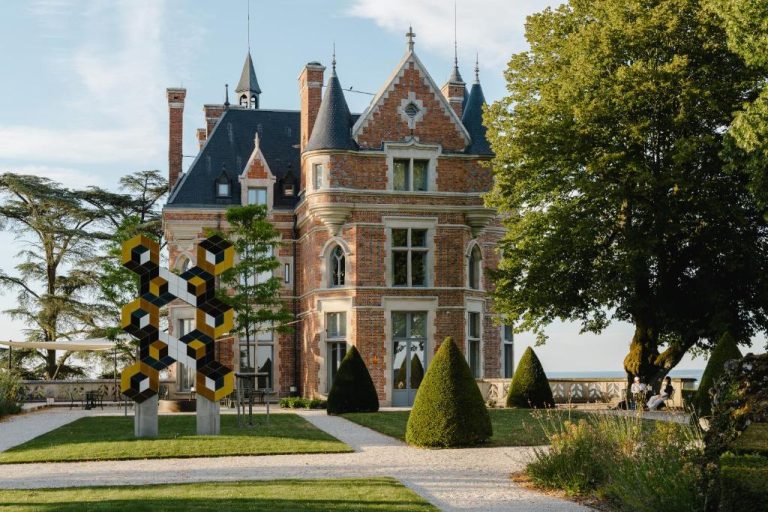 Fachada del castillo de Les Hauts de Sancerre con jardines y escultura moderna en primer plano