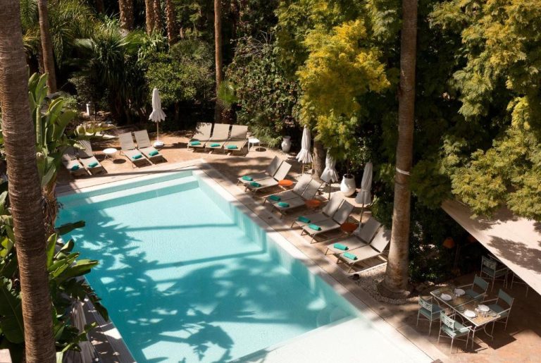 Piscina exterior rodeada de jardines tropicales con tumbonas en Les Jardins de la Médina