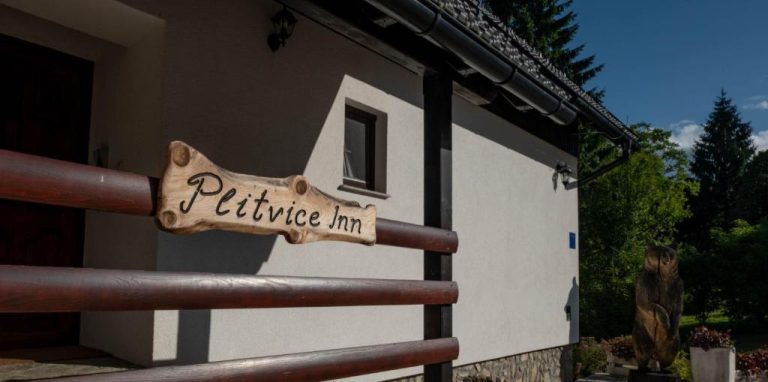 Cartel de madera artesanal en la entrada del Plitvice Inn rodeado de naturaleza y jardín