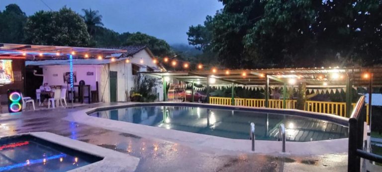 Piscina exterior iluminada de noche en Hotel Villas del Valle con zona de descanso y pérgola