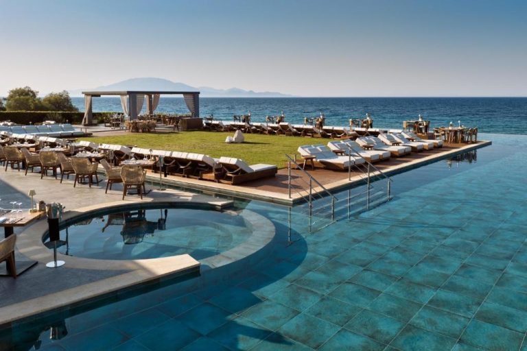 Piscina infinita con tumbonas y zona de restaurante frente al mar en Lesante Blu Adults Only