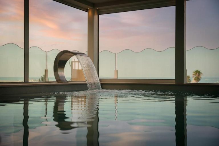 Spa interior con cascada de acero y vistas al mar al atardecer en el Savoia Hotel Rimini