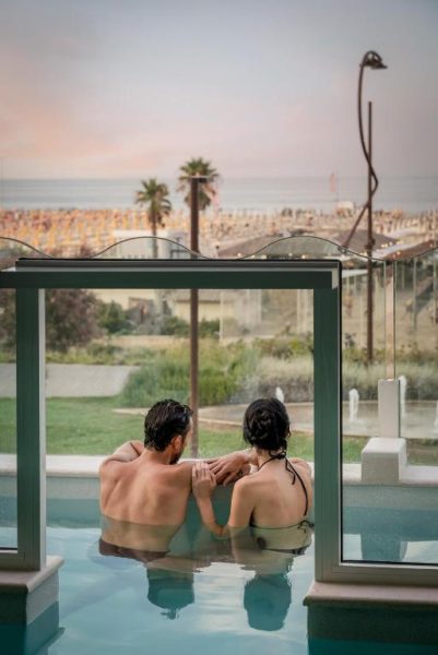 Pareja relajándose en jacuzzi exterior con vistas a la playa al atardecer en Savoia Hotel Rimini