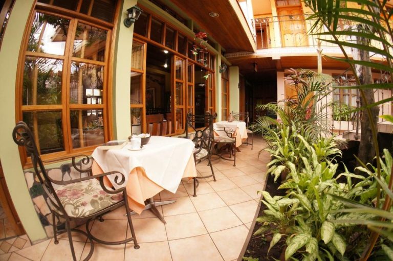 Terraza exterior con mesas y sillas de hierro forjado rodeada de plantas tropicales en Hotel Cafe