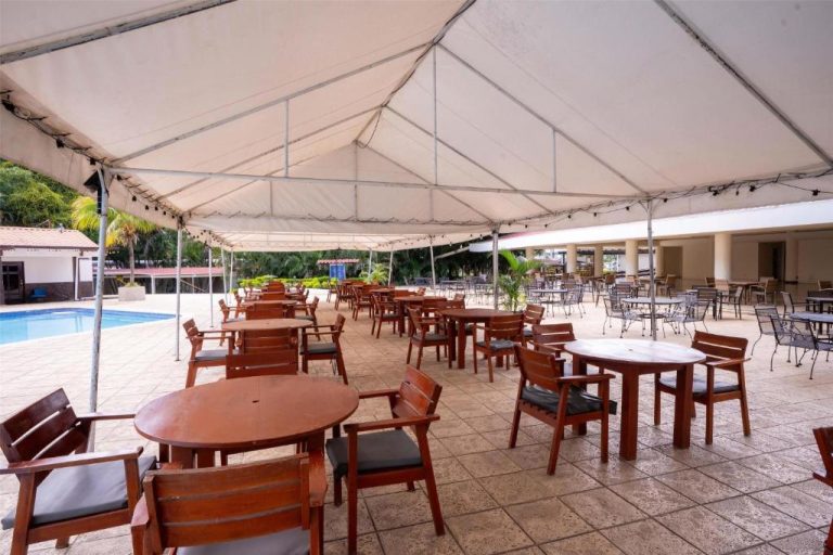 Terraza restaurante al aire libre con mesas de madera y piscina en Best Western Las Mercedes Airport