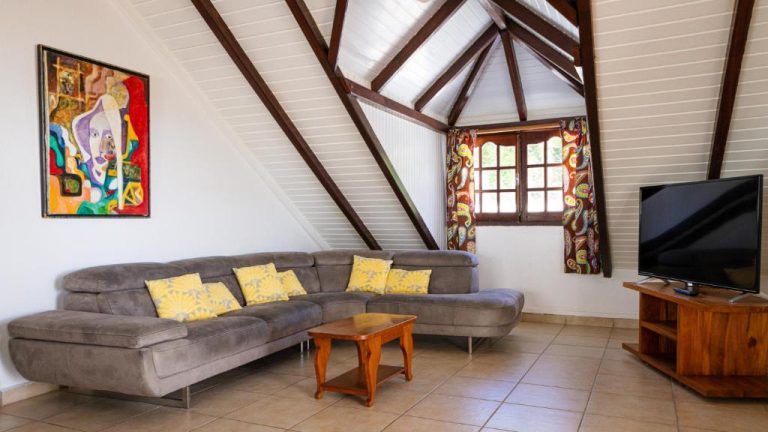 Salón con sofá rinconera gris y vigas de madera en buhardilla del Hôtel Le Soleil Levant