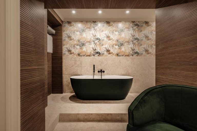 Bañera exenta negra con revestimiento mármol y sillón verde en suite de Sterling Luxury Suites Valletta