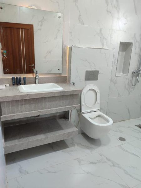 Baño moderno con mármol blanco, inodoro suspendido y lavabo empotrado en Oasis Majan Hotel