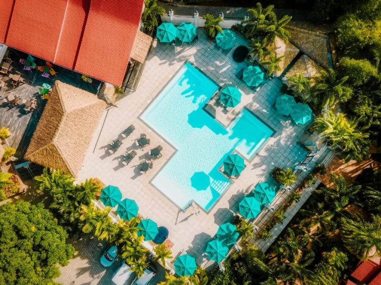 Vista aérea de la piscina exterior con sombrillas turquesas y tumbonas del Hotel Bambou rodeada de palmeras