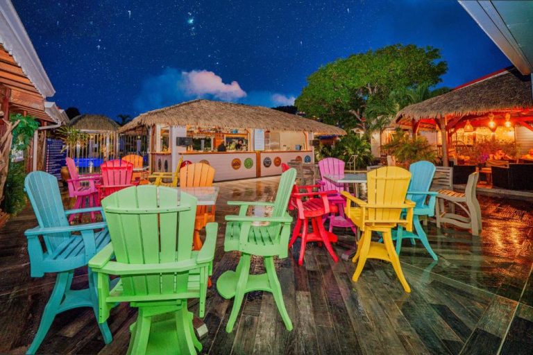 Terraza del Hotel Bambou con sillas Adirondack de colores y bar tiki iluminado por la noche
