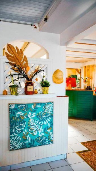 Recepción del Hotel Oasis con decoración tropical, plantas y cuadro de hojas en tonos turquesa