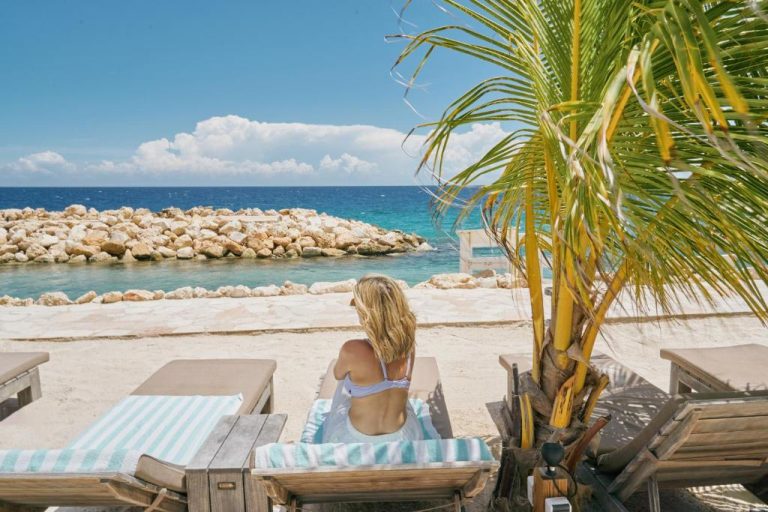 Mujer tomando el sol en tumbonas frente a la playa y el mar turquesa del Scuba Lodge City Beach