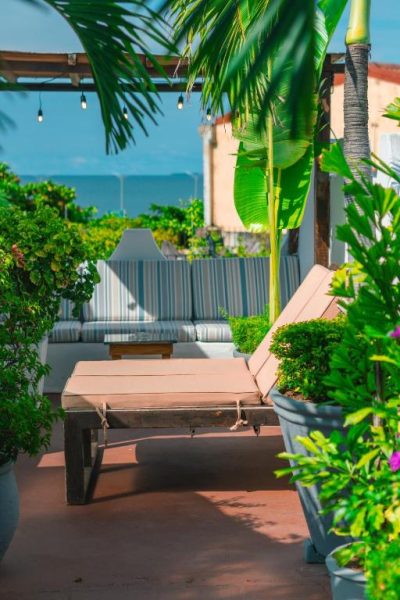 Terraza tropical con tumbonas y sofás del Hotel Kartaxa, rodeada de palmeras y plantas con vistas al mar