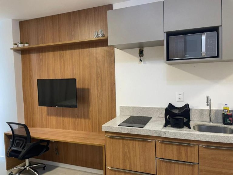 Cocina equipada con microondas, encimera de granito y TV en Luxuoso Flat Salvador Corredor da Vitoria