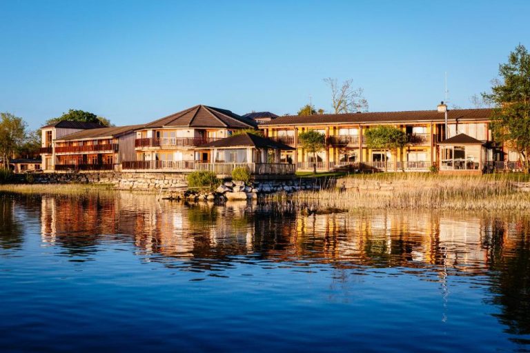 Vista exterior del Wineport Lodge reflejada en el lago con terrazas y balcones al atardecer