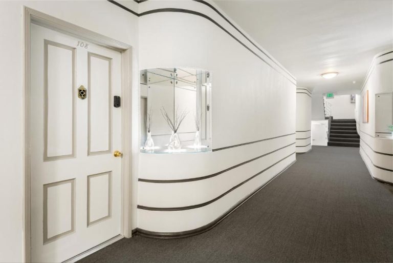 Pasillo blanco con decoración art déco y puerta de habitación 108 en el Beverly Grove Hotel