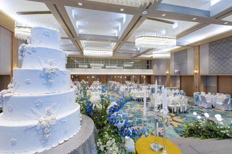 Elegante salón de bodas con pastel nupcial blanco y decoración floral azul en Phuket Merlin Hotel