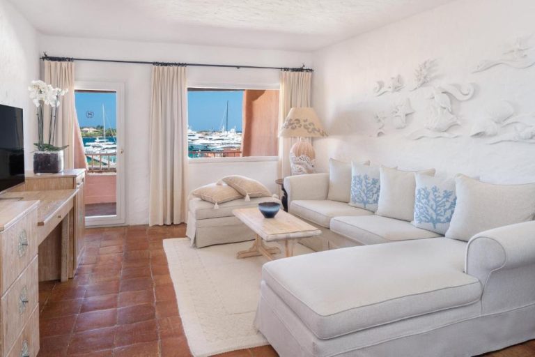 Salón elegante con sofás blancos y vistas al puerto deportivo en Cervo Hotel Costa Smeralda Resort