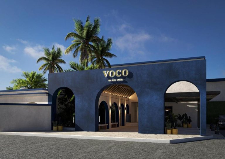 Fachada principal del hotel Voco Surfside Aruba con arcos azules y palmeras tropicales en Aruba