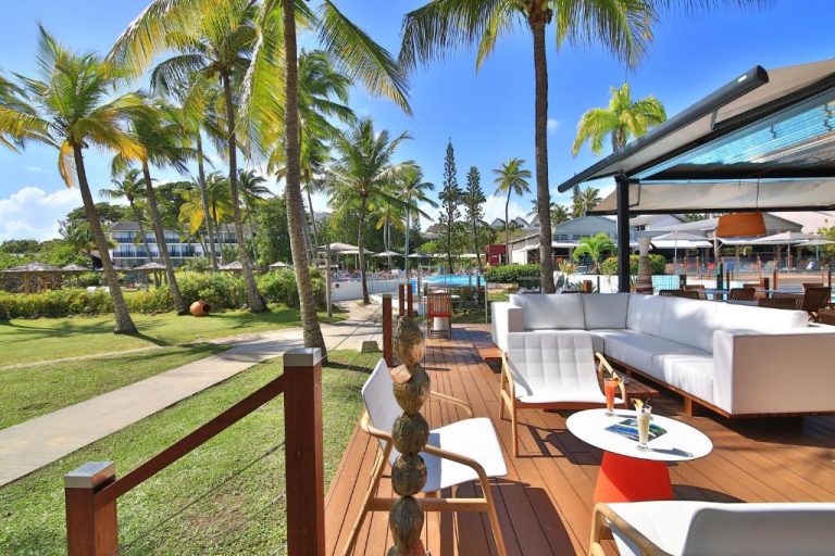 Terraza lounge con sofás blancos y vistas a la piscina rodeada de palmeras en Mahogany Hotel Residence & Spa