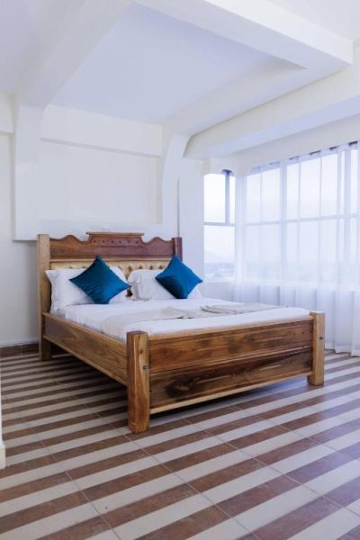 Habitación con cama de madera tallada y cojines azules en Isiolo Landmark Hotel