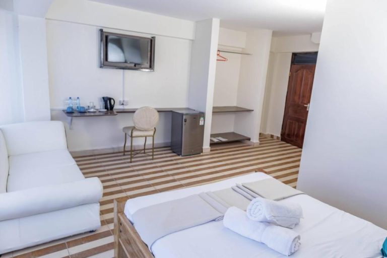 Habitación doble con sofá blanco, televisión, escritorio y frigorífico en Isiolo Landmark Hotel