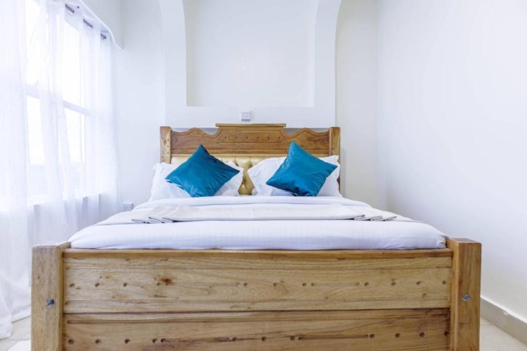 Habitación doble con cama de madera y almohadas azules en Isiolo Landmark Hotel