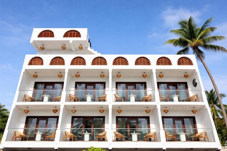 Fachada exterior del Palma De Maldives con balcones privados, sillas y palmeras tropicales bajo cielo azul