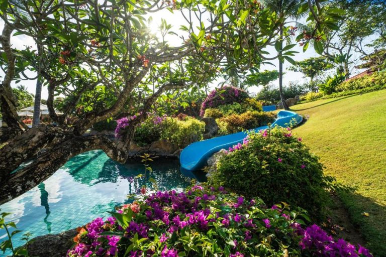 Piscina con tobogán azul rodeada de jardines tropicales y buganvillas en el Grand Hyatt Bali