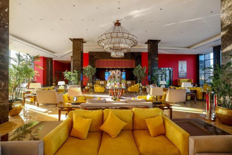 Lujoso lobby del Porto Said Hotel & Spa con sofás amarillos, lámpara de araña y decoración en rojo