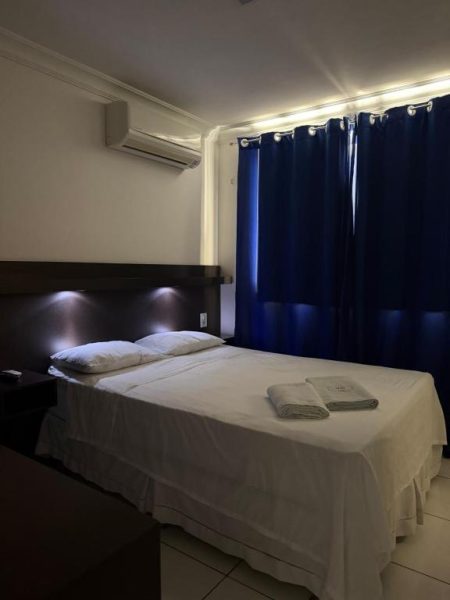 Habitación doble con cama matrimonial y cortinas azules en Hotel Sol Brasil