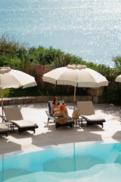 Turista leyendo junto a la piscina con tumbonas y sombrillas del Gabbiano Azzurro Hotel & Suites con vistas al mar