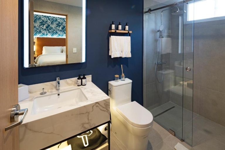Baño moderno con ducha de cristal y pared azul en el hotel voco Surfside Aruba by IHG