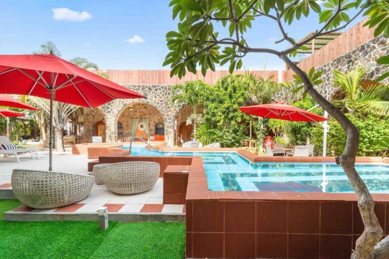 Piscina infinita con tumbonas y sombrillas rojas en el Aroma Plaza Boutique Hotel, rodeada de jardines