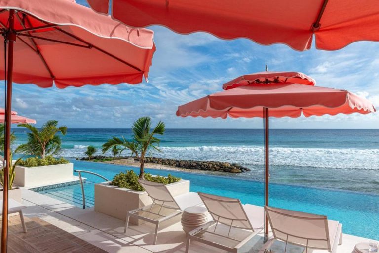 Piscina infinita con tumbonas y sombrillas rojas frente al mar en Hotel Indigo Bridgetown Barbados