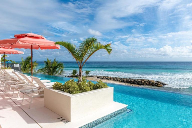 Piscina infinita con vistas al mar Caribe del Hotel Indigo Bridgetown Barbados con tumbonas y sombrillas rosas