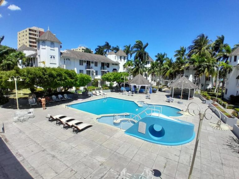 Piscina exterior con tobogán y hamacas del resort Sandcastles en Jamaica rodeada de palmeras