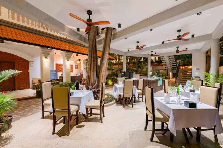 Restaurante al aire libre con mesas elegantes y árbol central en The Sears Residence Siem Reap