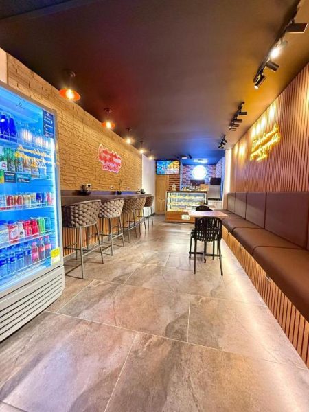 Bar cafetería interior del Hotel Nakama con nevera de bebidas, zona lounge y barra de bar iluminada