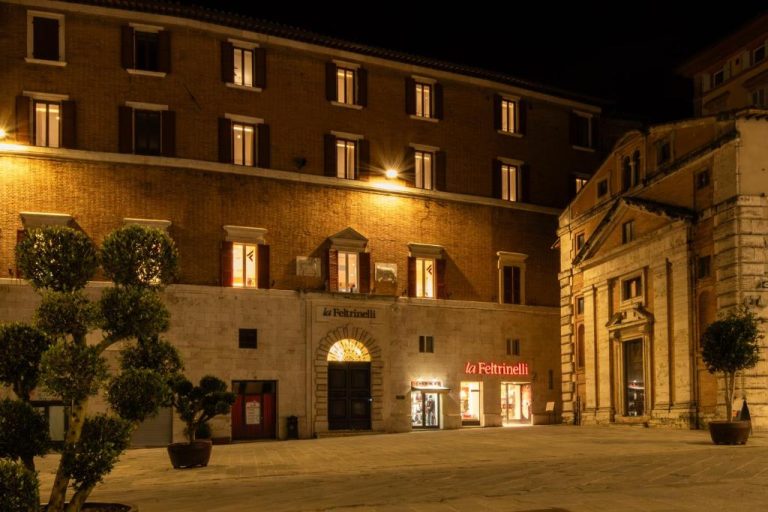 Fachada nocturna del The Bank Hotel Etruria Collection con tienda La Feltrinelli iluminada