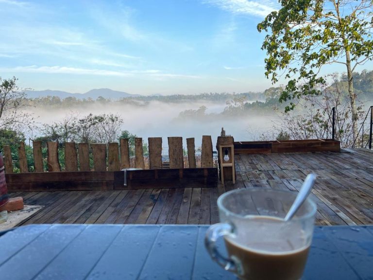 Terraza de madera con vista panorámica a la niebla y montañas del hotel Le VyN Mang Den con café