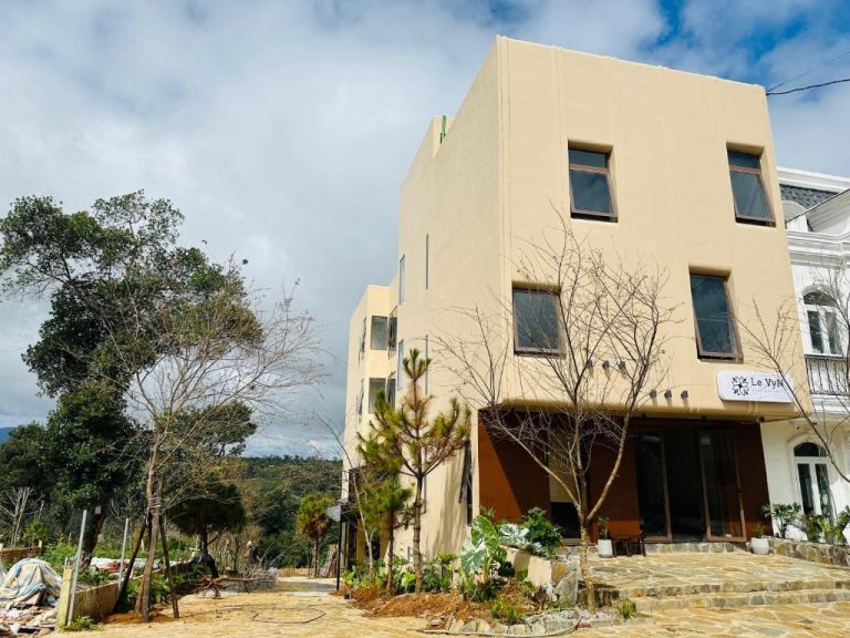 Fachada exterior del Hotel Le VyN Mang Den rodeada de árboles y jardines en construcción