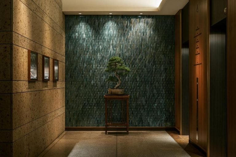 Entrada del The Aoyama Grand Hotel con bonsái decorativo sobre mesa de madera y pared de mármol verde
