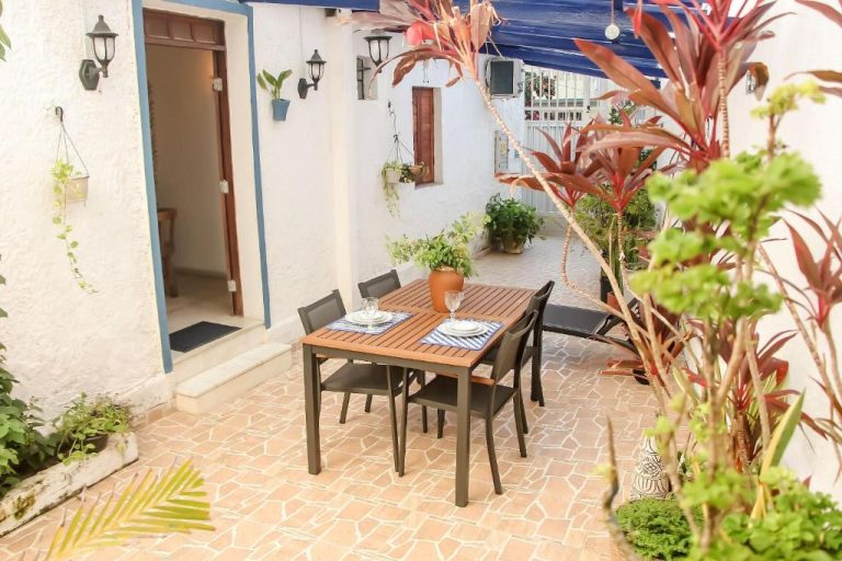 Terraza exterior con mesa de madera y sillas en Pousada Maria Maria rodeada de plantas tropicales